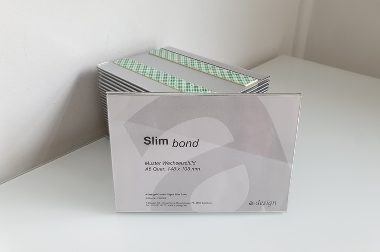 Schild Slim Bond mit beispielhaftem Papiereinzug und Stapel von Schilder im Hintergrund.